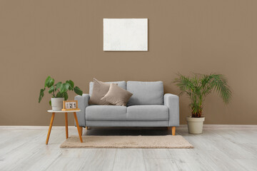 Stylish grey sofa, houseplants and picture hanging on light wall in living room