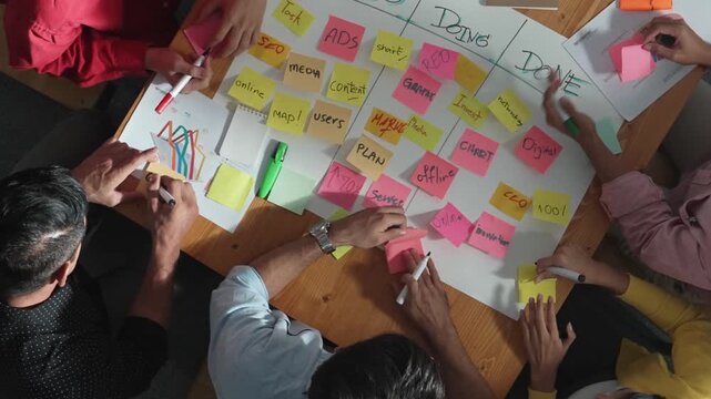 Top view of people writing and making scrum task board while writing marketing and planning strategy at colorful sticky notes. Smart team manage work performance by using kanaban board. Convocation.