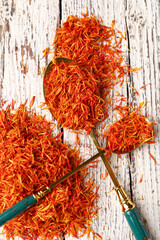 Spoons with pile of saffron on white wooden background