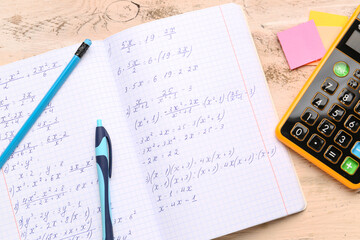 Copybook with maths formulas, calculator and stationery on beige wooden background