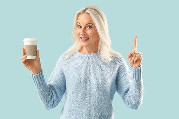 Mature woman with takeaway cup of coffee pointing at something on blue background