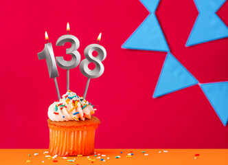 Number 138 candle with birthday cupcake on a red background with blue pennants