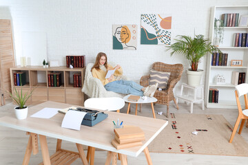 Fototapeta premium Female author with book sitting in armchair at home