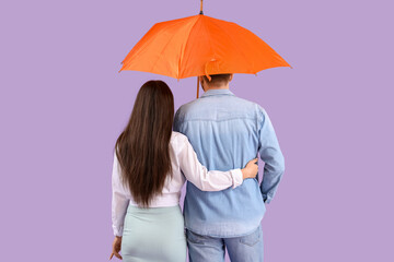 Young couple with opened umbrella walking on lilac background, back view