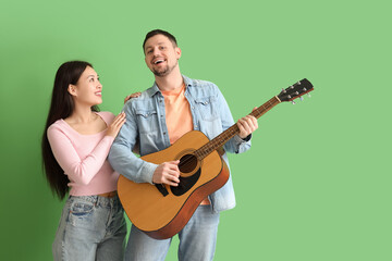 Young man playing guitar for his girlfriend on green background