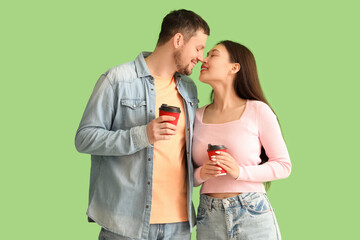 Young couple kissing and holding cups of coffee on green background