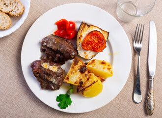 Delicious grilled pork cheeks served on rustic plate with side of roasted potatoes, tomato, eggplant and pepper for dinner. Traditional Spanish dish