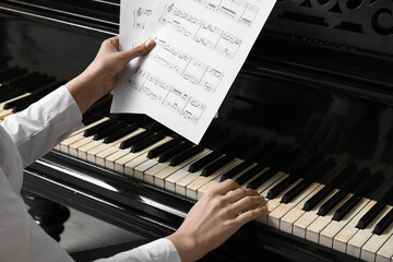 Young woman playing piano with note sheet © Pixel-Shot