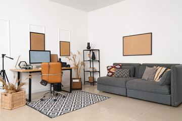 Stylish workplace with modern computer, and photographer's equipment and sofa near white wall in light office