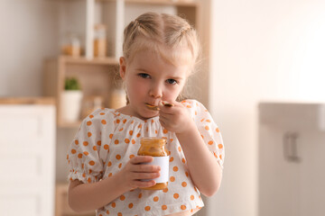 Cute little girl with spoon eating jam at home