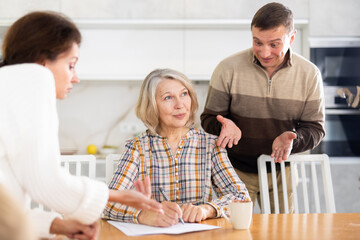 Competitive middle-aged man and woman conflicting and old woman writing inheritance sitting at...