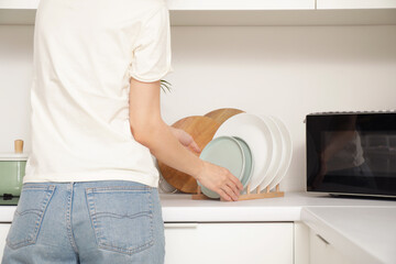 Young woman putting dishes near microwave on counter in kitchen