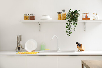 Stack of white clean plates and cutlery near sink on counter in kitchen