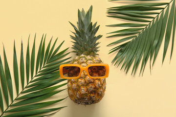 Fresh pineapple with sunglasses and palm leaves on yellow background