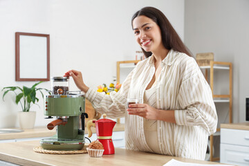 Pretty young woman with cup of hot espresso and coffee maker at home