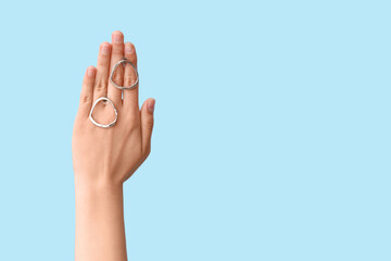 Female hand with beautiful silver earrings on blue background