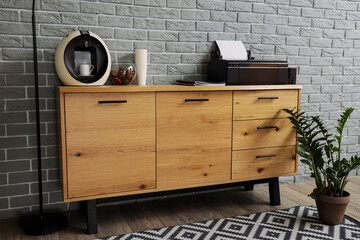 Modern printer and coffee machine on commode near grey brick wall in office