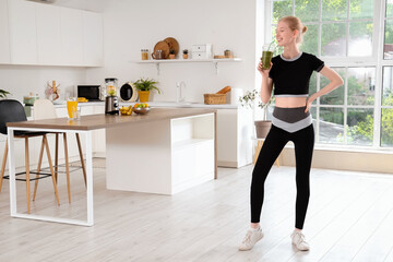 Happy sporty young woman with healthy smoothie in kitchen