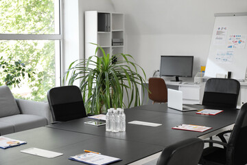 Interior of modern conference hall with big table, armchairs, shelving unit and houseplant, closeup