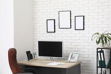 Interior of stylish office with workplace, armchair, modern computer and shelving unit
