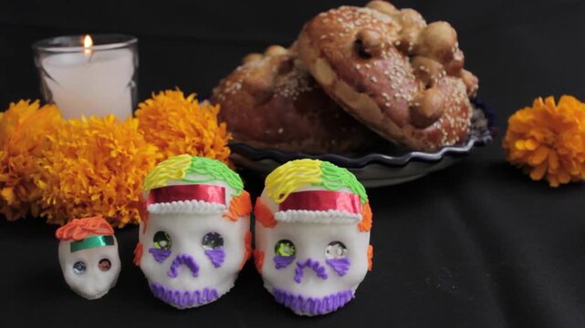 Acercamiento a calaveras de az&uacute;car en ofrenda de d&iacute;a de muerrtos, roeado de flores, pan, y ducles t&iacute;pcos