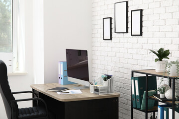 Interior of light office with workplace, armchair, modern computer and shelving unit