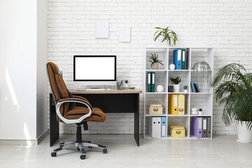 Interior of light office with workplace, armchair, modern computer and shelving unit