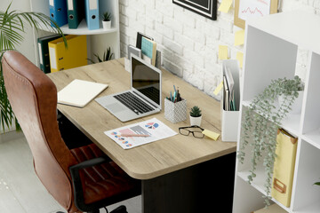 Interior of office with workplace, brown armchair, modern laptop and shelving unit, closeup