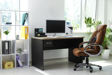 Interior of office with workplace, armchair, modern computer and shelving unit