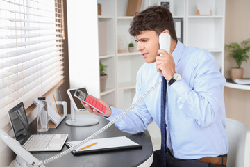 Male accountant working with calculator and talking on phone at workplace in office