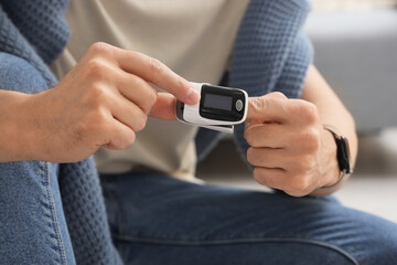 Young man with pulse oximeter at home, closeup