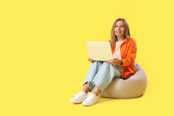 Naklejka premium Mature woman with laptop sitting on beanbag against yellow background