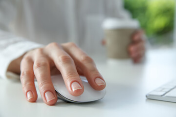 Fototapeta premium Woman with wireless mouse and paper cup at white table indoors, closeup