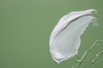 Face cream and gel on green background, top view. Space for text