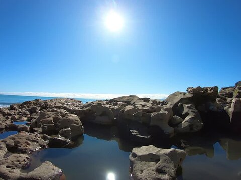 Reflection in water in the rock formations at the beach on the sunny day 