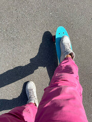 Close up of feet of a girl in white sneakers rides on blue plastic penny skate board with pink...