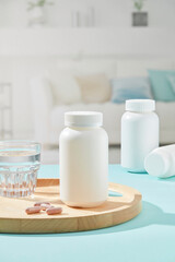 Creative scene for advertising with pharmacy theme. A white bottles container medicine displayed on blue table with wooden tray and glass cup. Front view, living room background