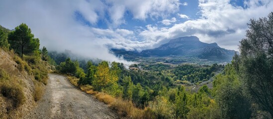 Panoramic mountain peak landscape with lush green valley, misty clouds, and winding road