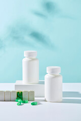 Front view of two white bottles unlabeled displayed on white podiums with medicine daily box and green capsules on blue background. Minimal style for advertising medicine product