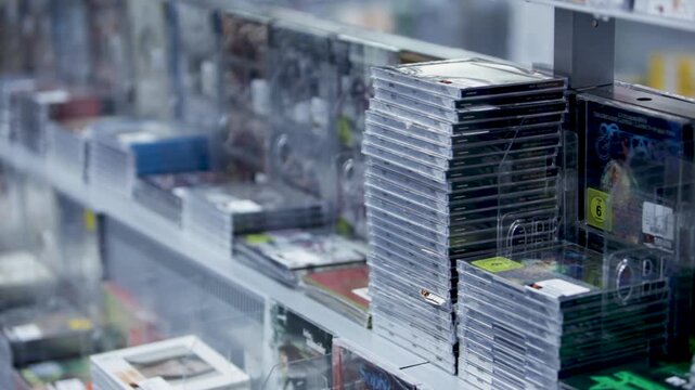 Stacked CDs on store shelves display various albums in clear cases, ready for purchase
