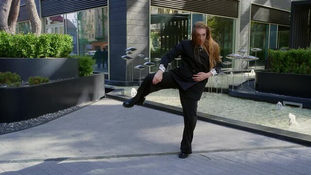 Contemporary dancer performing by modern art and fountain. Full length of young woman with long hair is dancing with building in background. She is wearing formals at public park on windy day.