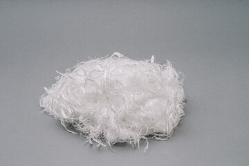 A tangled ball of white fiberglass fibers with a fluffy texture, placed on a grey background. The...