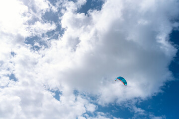 paraglider soars high above sunny sky filled with fluffy clouds on clear day