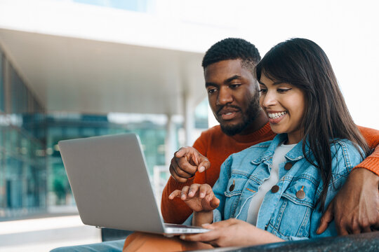 Couple Engaged in Laptop Discussion Outdoors at Modern Cafe on Sunny Day