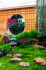 Minimal Japanese garden in home with small stone lantern and bamboo fountain and moss and flowers.

