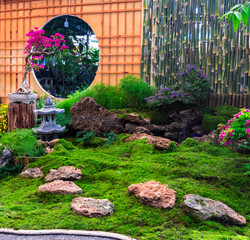 Minimal Japanese garden in home with small stone lantern and bamboo fountain and moss and flowers.


