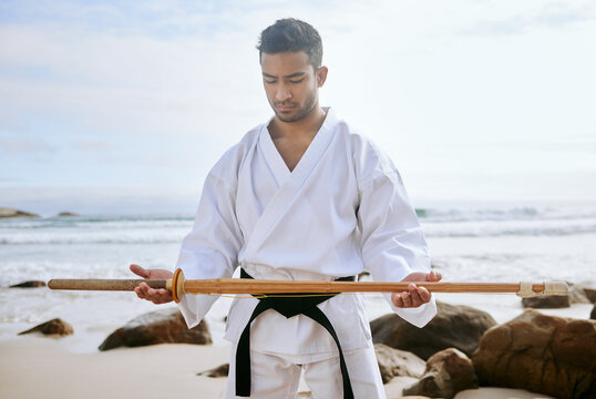 Asian man, karate and beach with wooden sword for martial arts, training or self defense in nature. Young male person, warrior or samurai with katana, weapon or uniform on ocean coast for taekwondo