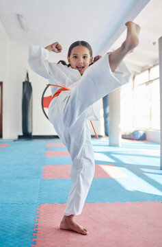 Martial arts, kick and girl in studio for fitness, training and fight with orange belt, development and energy. Student, kung fu and portrait in dojo as workout for self defense, karate and taekwondo