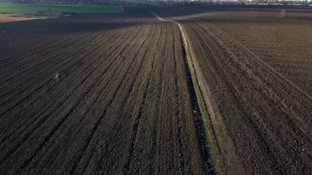 Flying over large plowed field of black soil. Field of dug up earth on autumn day. Aerial view of plowed farmland, agricultural lands. Ground land earth. Natural agricultural industrial background