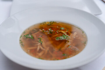 Hot and Savory Soup Served in White Bowl, Garnished With Herbs and Thinly Sliced Vegetables, on White Tablecloth